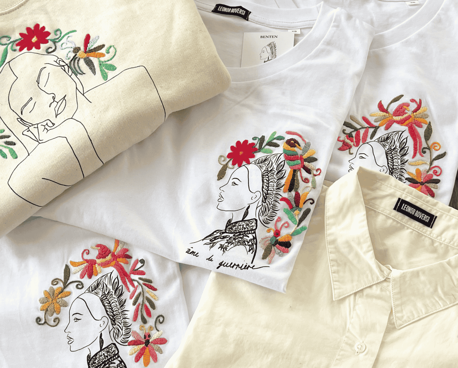 Trois pièces Leonor Roversi posées sur une table : t-shirts et sweat en coton biologique brodés à la main au Mexique. Les broderies artisanales représentent des visages féminins entourés de fleurs colorées, symbolisant l’artisanat mexicain et l’engagement de la marque.