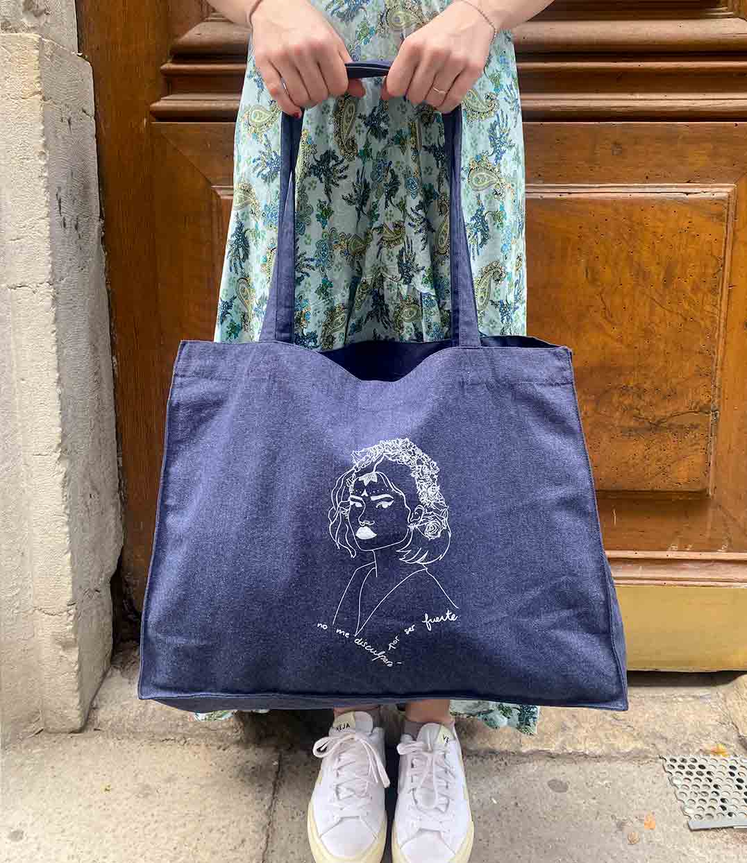 Sac cabas en coton bio denim avec un imprimé blanc représentant une femme forte inspirée d’une reine d’Amérique latine, accompagné de l’inscription “No me disculparé por ser fuerte”. Modèle Lupita, conçu et imprimé à Lyon par la marque éthique Leonor Roversi.