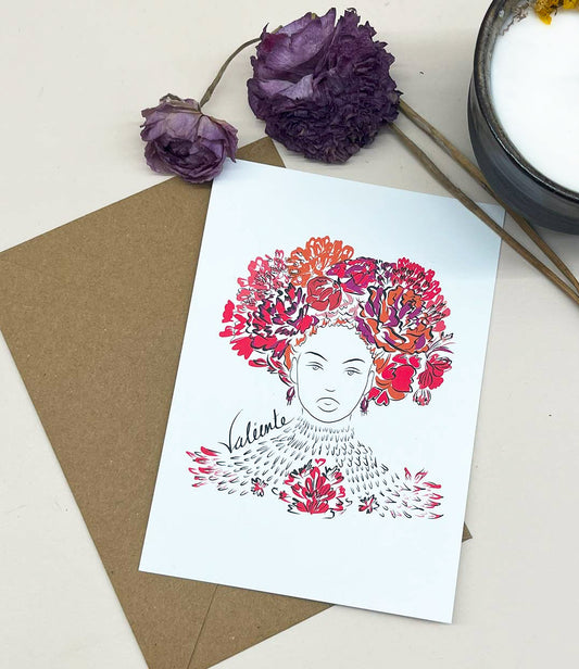 Carte postale illustrée d'une femme forte avec des fleurs rouges et oranges dans les cheveux représentant la première reine nigériane accompagnée de l'inscription  "Valiente" sur le côté. Modèle Valiente, conçue et imprimée à Lyon par la marque éthique Leonor Roversi.