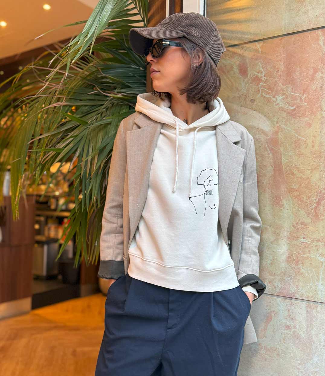 Femme portant un hoodie en coton bio écru, imprimé noir d'une femme forte avec l'inscription "battante" porté avec un blazer beige. Modèle Klimt, conçu et imprimé à Lyon par la marque éthique Leonor Roversi.