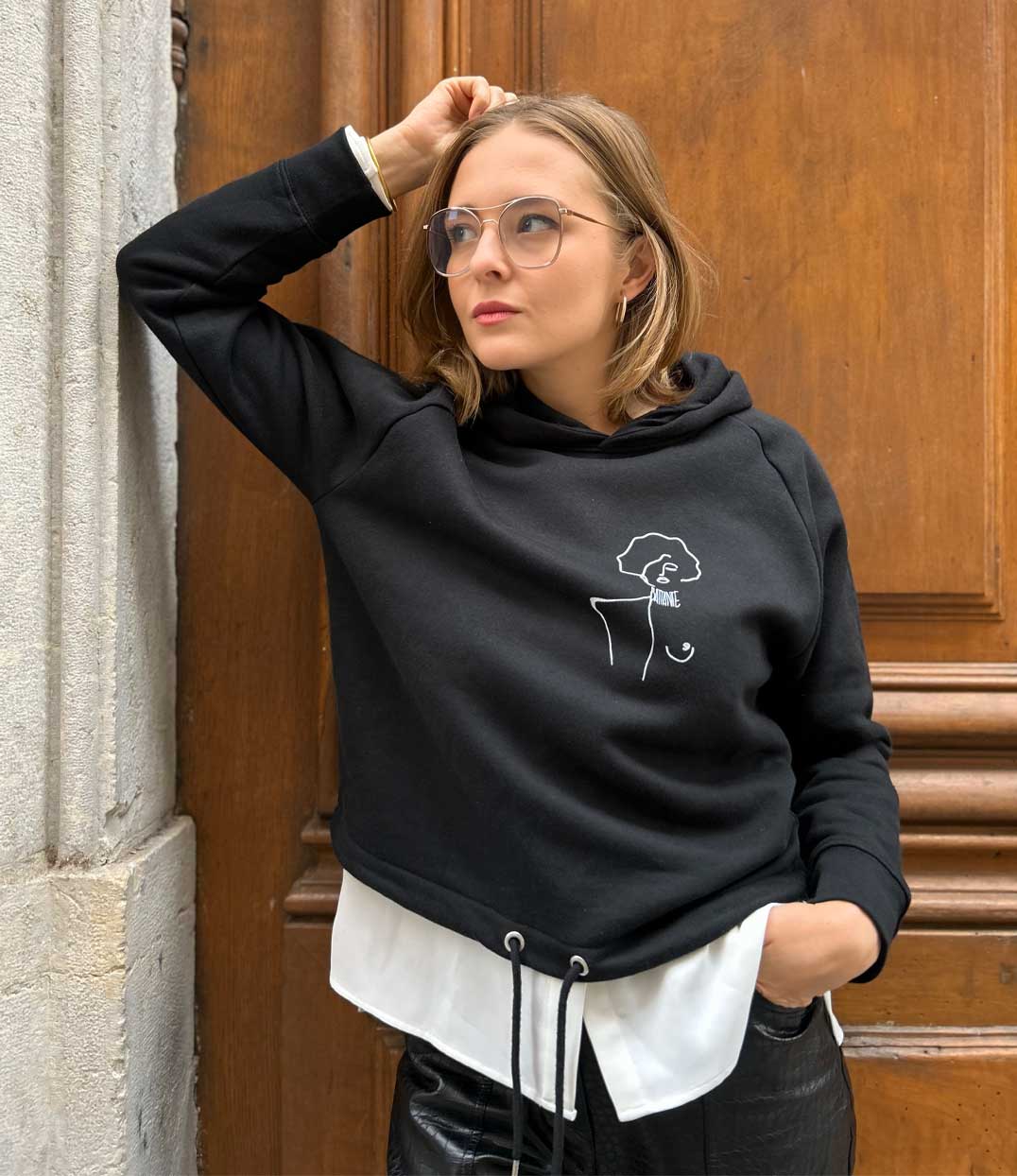 Portrait d’une femme portant le hoodie noir “Gozen” de Leonor Roversi, orné d’un dessin minimaliste représentant une figure féminine affirmée. Vêtement en coton bio sérigraphié à la main, symbole de féminisme, de créativité et d’engagement pour une mode éthique.