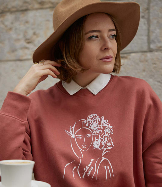 Sweatshirt en coton bio terracotta, imprimé blanc d'une femme au regard serein entourée de fleurs dans les cheveux accompagnée de l'inscription "Absolumente única". Modèle Unica, conçu et imprimé à Lyon par la marque éthique Leonor Roversi.