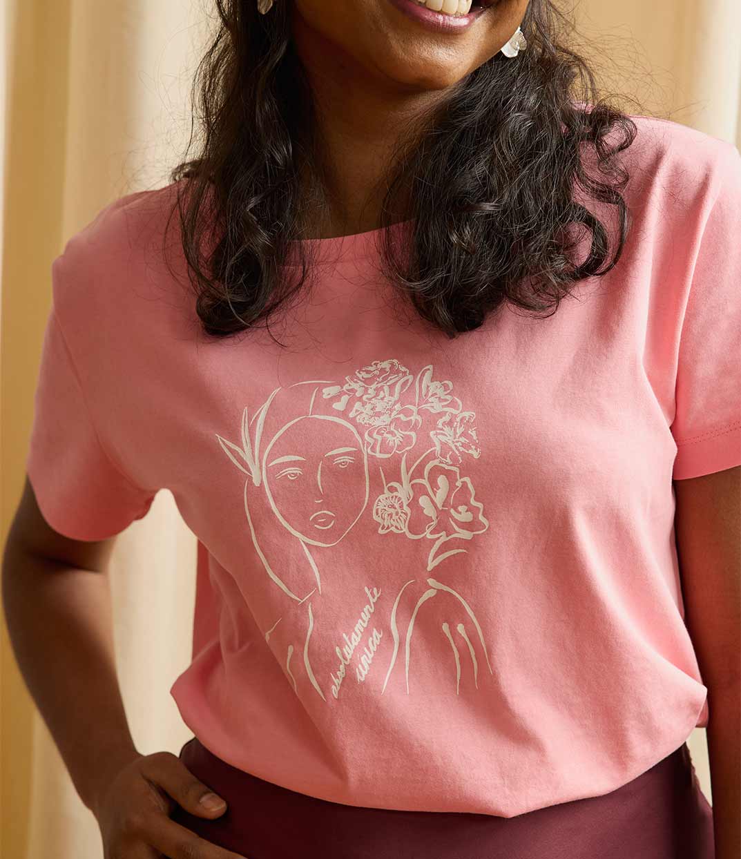 Une femme inspirante portant un t-shirt rose Unica de Leonor Roversi, marque de mode inclusive et éthique basée à Lyon, en coton biologique et sérigraphie artisanale, mettant en valeur une illustration inspirée de Mary Cassatt qui célèbre la singularité, la douceur et la force féminine.