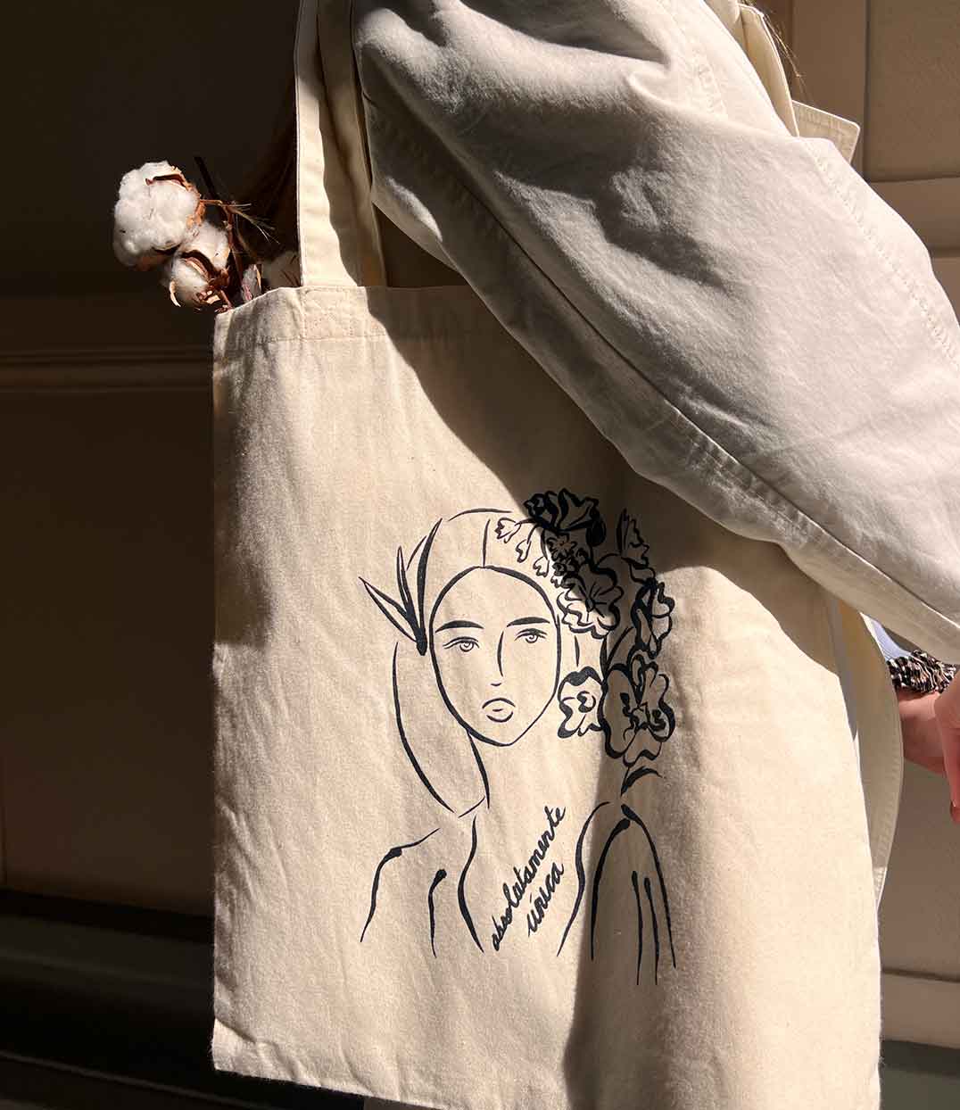 Tote bag naturel Leonor Roversi en coton biologique, orné de l’illustration "Unica" et de la phrase « absolutamente única ». Accessoire éthique et artistique célébrant la singularité féminine, confectionné avec soin dans une démarche de mode durable.