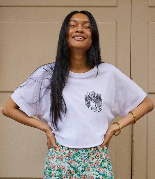 T-shirt pour femme en coton bio blanc. Il présente un imprimé noir représentant une figure de samouraï couronnée de fleurs, accompagné de l’inscription « âme d’une conquérante ». Modèle Gozen, conçu et imprimé à Lyon par la marque éthique Leonor Roversi.