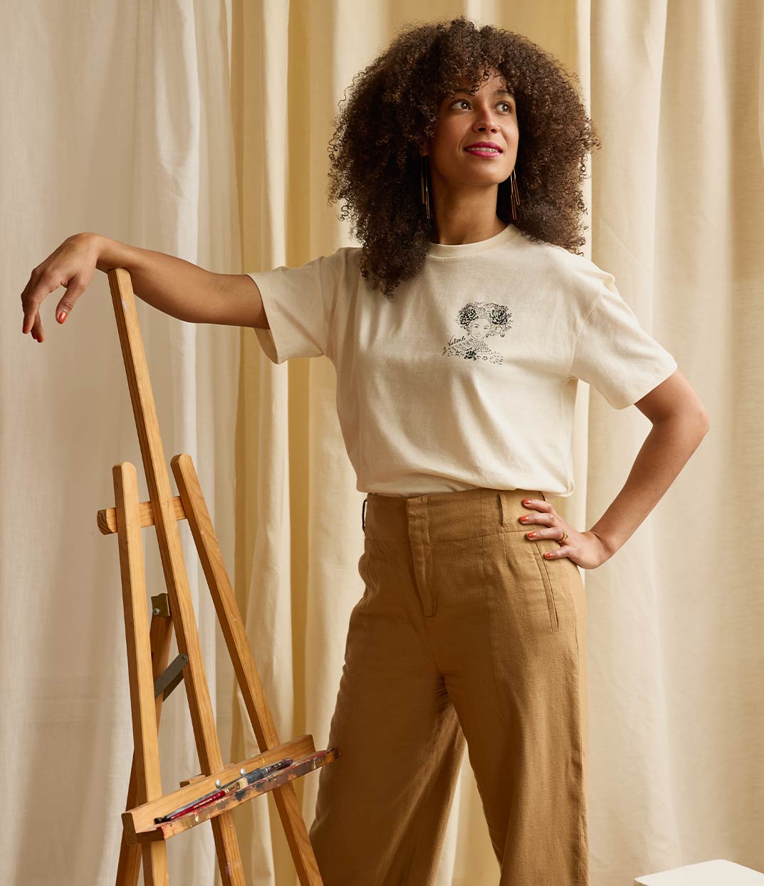 Femme rayonnante portant le t-shirt Valiente écru de la marque Leonor Roversi. Inspiré de la reine nigériane Amina de Zaria, ce visuel rend hommage à une femme conquérante et courageuse. Une pièce de mode responsable et engagée, produite localement et imprimée en sérigraphie artisanale dans une démarche de savoir-faire français.