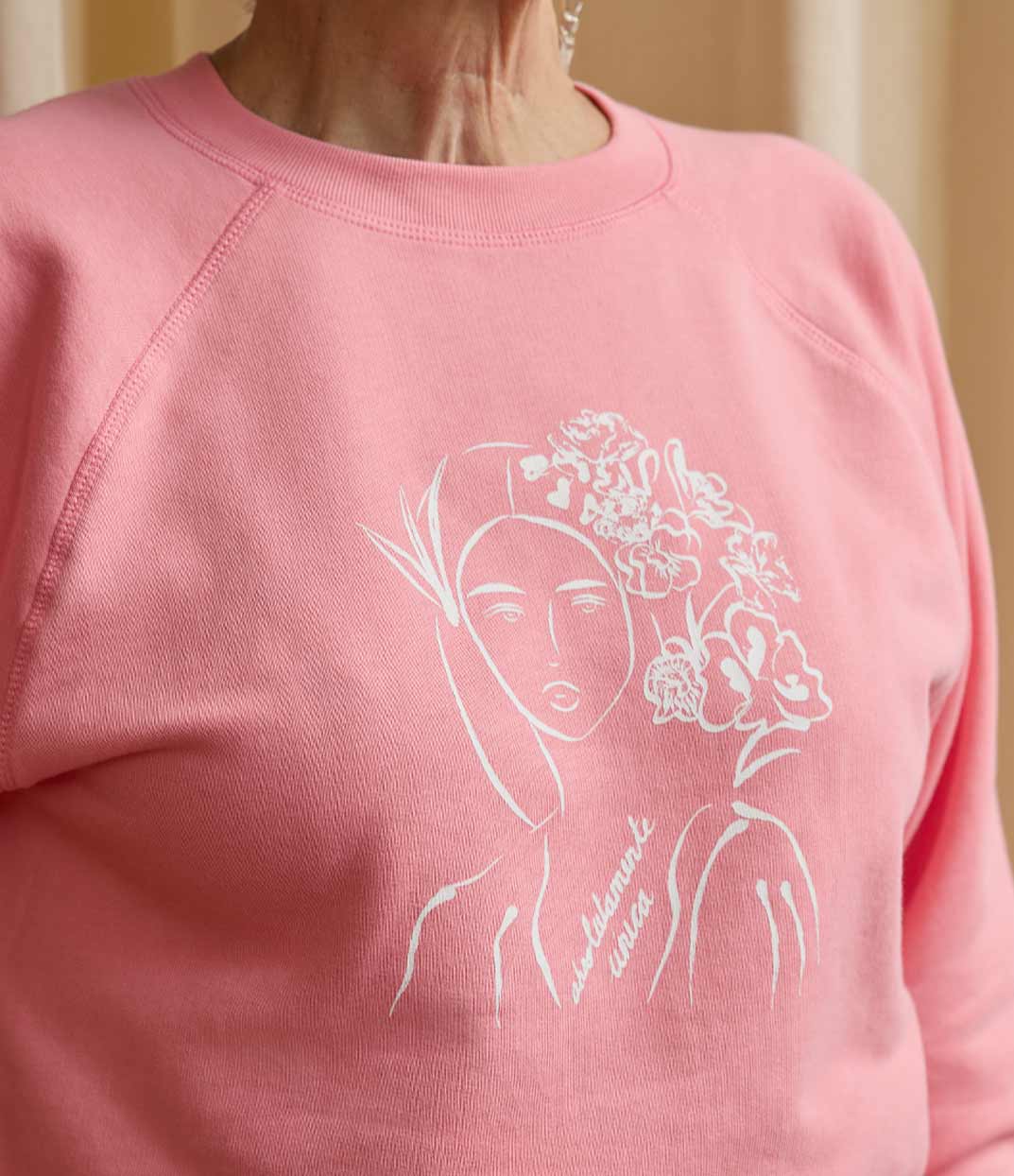 Gros plan sur une femme portant un sweatshirt rose Unica en coton biologique de Leonor Roversi, marque lyonnaise de mode inclusive et artistique, avec une illustration inspirée de Mary Cassatt mettant à l’honneur la beauté unique et intemporelle de chaque femme.