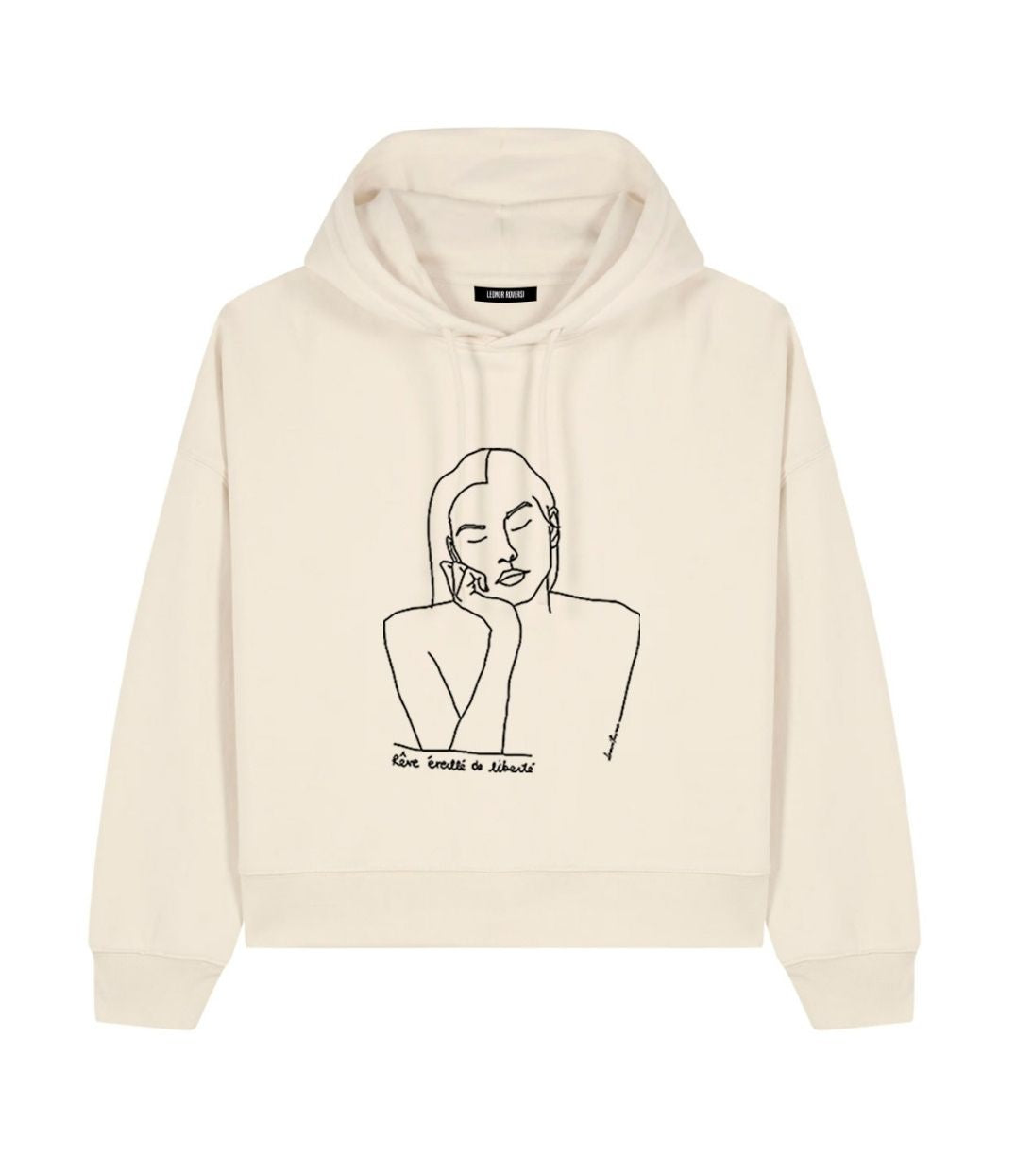 Mock-up d'un hoodie pour femme ample en coton bio écru. Le vêtement présente un imprimé noir minimaliste d’un visage féminin aux yeux clos, accompagné de l’inscription « rêve éveillé de liberté ». Modèle Thémis, conçu et imprimé à Lyon par la marque éthique Leonor Roversi.
