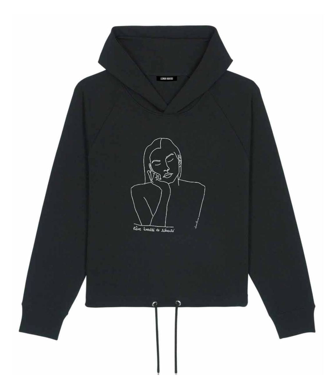 Mock-up d'un hoodie pour femme en coton bio noir. Le vêtement présente un imprimé blanc minimaliste d’un visage féminin aux yeux clos, accompagné de l’inscription « rêve éveillé de liberté ». Modèle Thémis, conçu et imprimé à Lyon par la marque éthique Leonor Roversi.