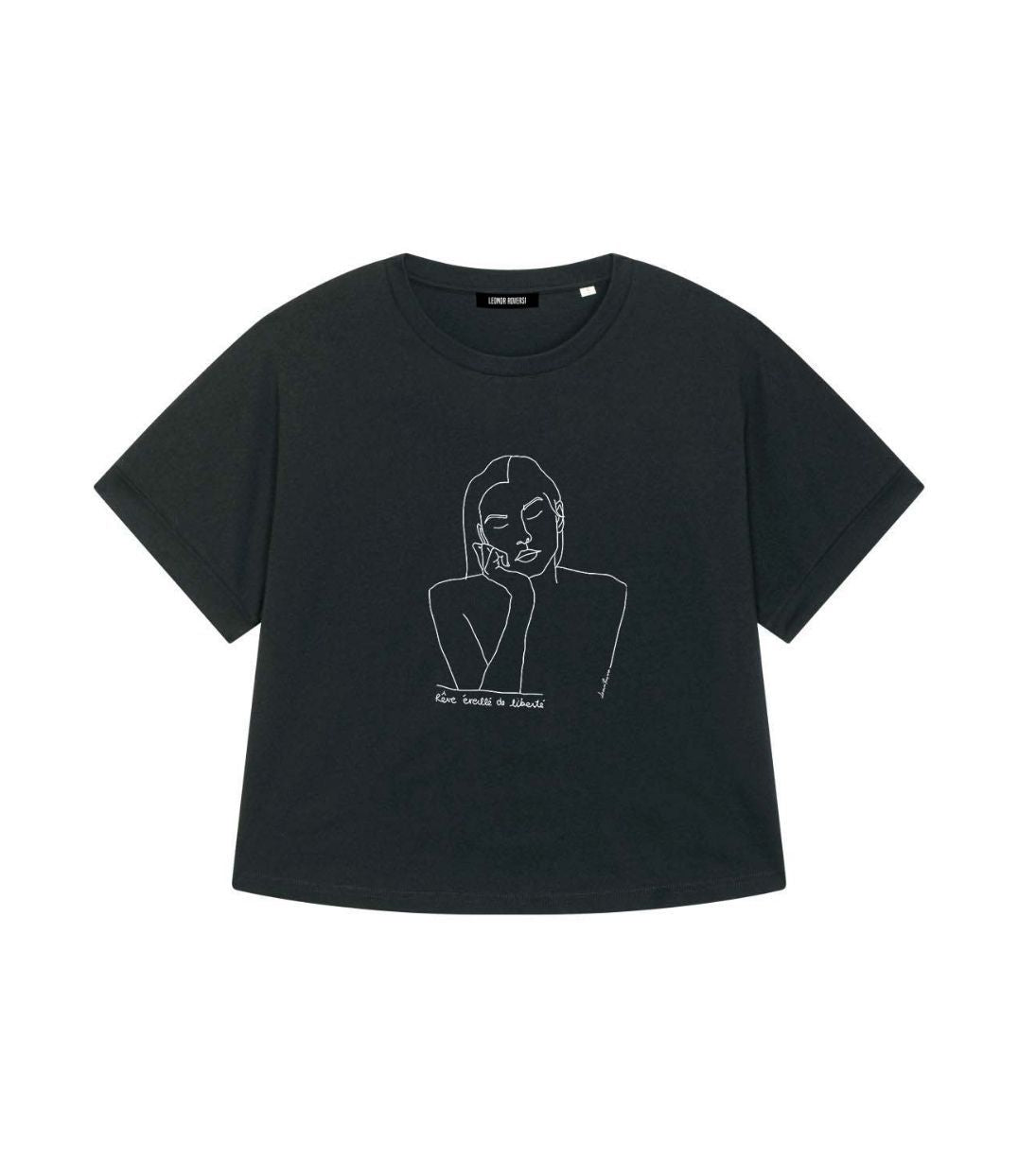 Mock-up d'un t-shirt pour femme ample en coton bio noir. Le vêtement présente un à l'avant, un imprimé blanc minimaliste d’un visage féminin aux yeux clos, accompagné de l’inscription « rêve éveillé de liberté ». Modèle Thémis, conçu et imprimé à Lyon par la marque éthique Leonor Roversi.