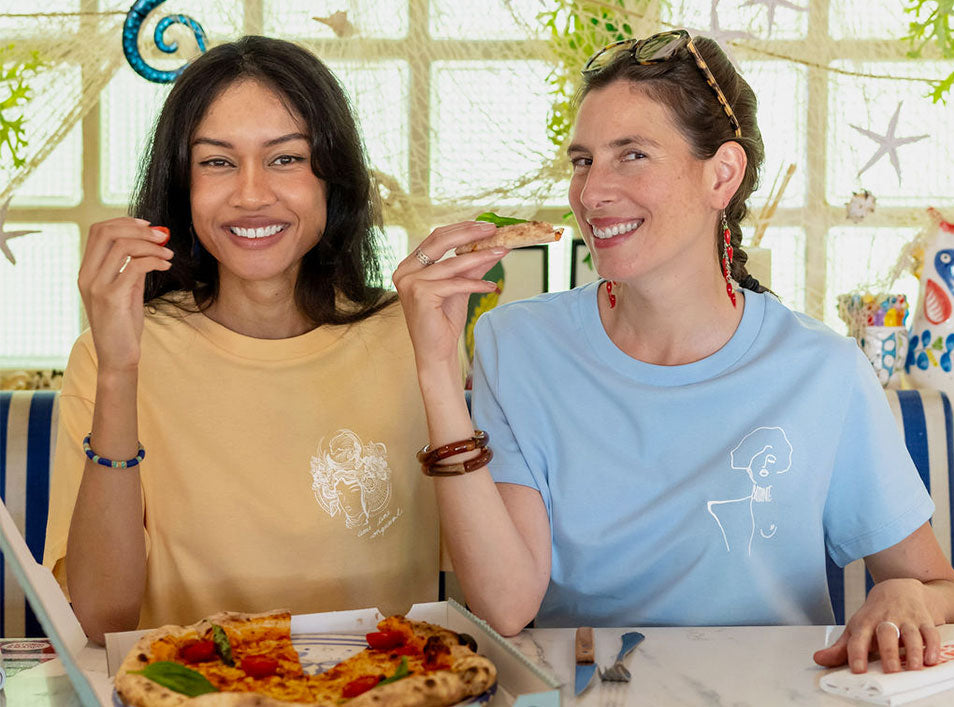 Deux femmes portant un t-shirt en coton bio couleur melon et bleu. Le t-shirt melon est accompagné d'un imprimé blanc représentant la plus grande femme samouraï avec l'inscription "âme d'une conquérante". Le t-shirt bleu présente un imprimé blanc représentant une femme qui a sauvé son village des flammes inspirée d'un tableau de Klimt avec l'inscription "Battante". Modèle Gozen et Klimt, conçu et imprimé à Lyon par la marque éthique Leonor Roversi.