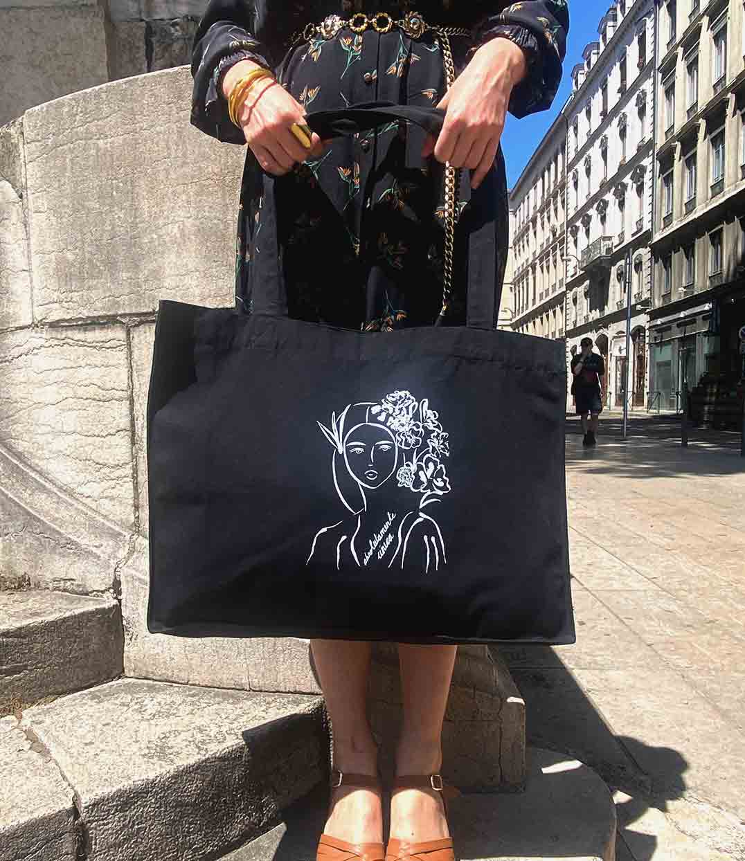 Sac cabas en coton bio noir, imprimé blanc d’une femme inspirée de la peintre impressionniste Mary Cassatt représentant une femme au regard serein entourée de fleurs dans les cheveux accompagnée de l'inscription "Absolumente única". Modèle Unica, conçu et imprimé à Lyon par la marque éthique Leonor Roversi.