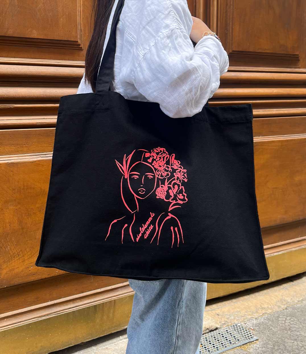 Cabas noir en coton bio avec imprimé rose illustrant une silhouette féminine avec des fleurs suivi de l'inscription "absolumente única". Modèle Unica, conçu et imprimé à Lyon par la marque éthique Leonor Roversi.