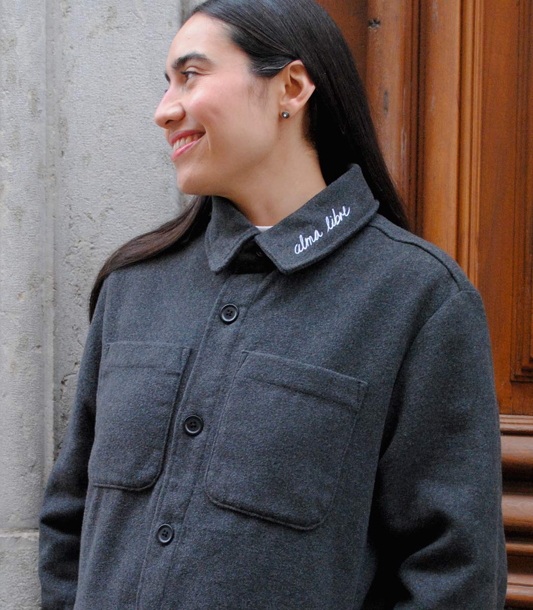 Veste ALMA LIBRE Leonor Roverssi en polyester recyclé certifié GOTS et FairWear, coupe droite gris foncé, portée par une femme confiante. Vêtement éthique brodé à Lyon, inspiré de la liberté intérieure et de la résilience féminine.