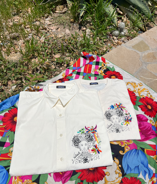 Chemise blanche et t-shirt écru Leonor Roversi brodés “Valiente”, posés au soleil sur un tissu fleuri coloré en extérieur.