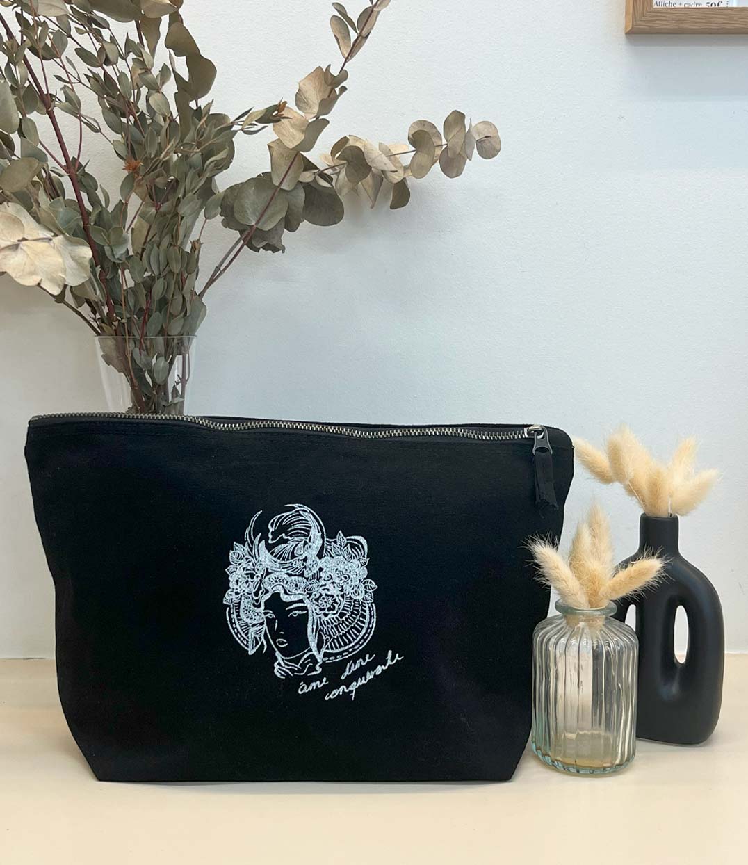 Grande pochette pour femme en coton bio noire. Il présente un imprimé blanc représentant une figure de samouraï couronnée de fleurs, accompagné de l’inscription « âme d’une conquérante ». Modèle Gozen, conçu et imprimé à Lyon par la marque éthique Leonor Roversi.