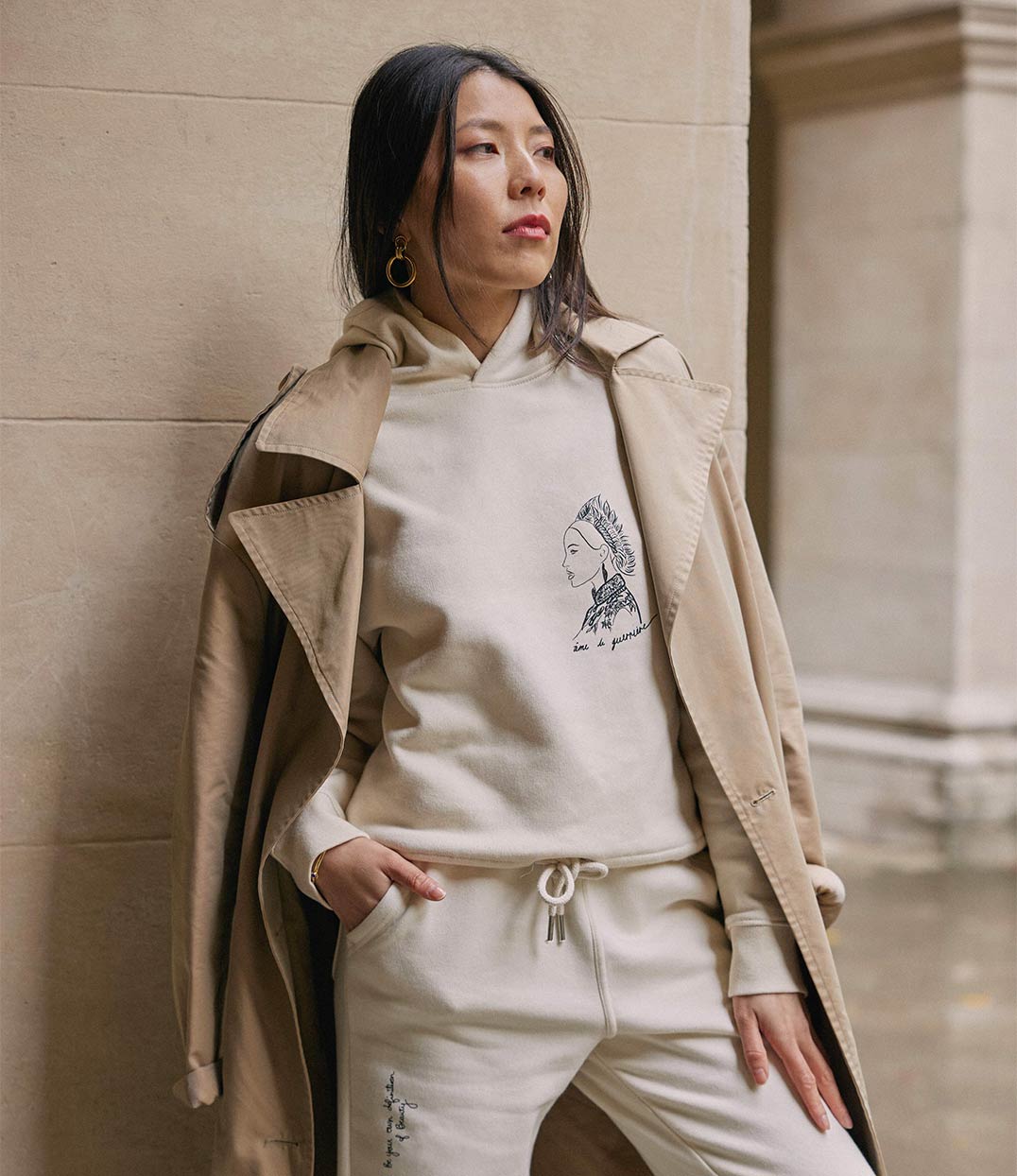 Femme portant un hoodie en coton bio écru. Le vêtement présente un imprimé noir représentant une guerrière japonaise, accompagnée de l’inscription « âme d'une guerrière ». Modèle Benten, conçu et imprimé à Lyon par la marque éthique Leonor Roversi.