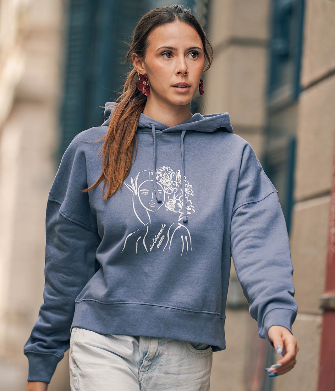 Mannequin femme, avec une queue de cheval, marche et porte un sweat-shirt à capuche en coton bio , bleu gris avec un dessin dessus, Leonor Roversi.