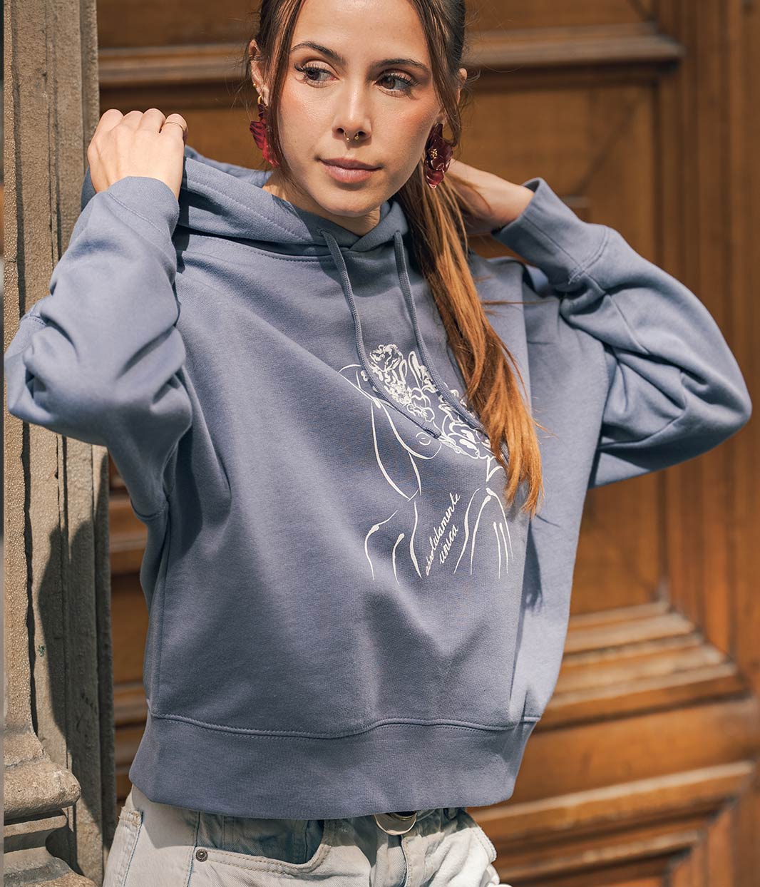 Mannequin femme, avec une queue de cheval, porte un sweat-shirt à capuche en coton bio , bleu gris avec un dessin dessus, Leonor Roversi.