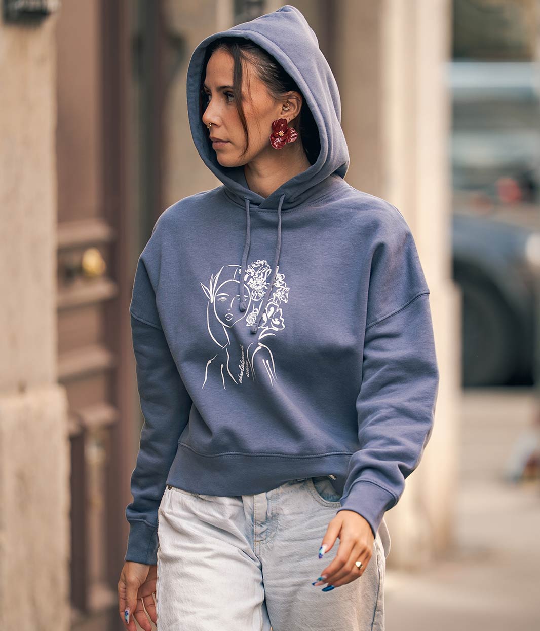 Mannequin femme, marche et porte la capuche de son sweat-shirt en coton bio , bleu gris avec un dessin dessus, Leonor Roversi.