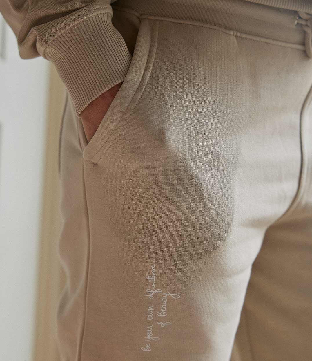 Pantalon de jogging femme en coton bio sable de Leonor Roversi, en coton biologique, avec l’inscription brodée « Be your own definition of beauty ». Pièce douce et confortable, pensée pour une mode responsable qui célèbre l’amour de soi et l’authenticité.