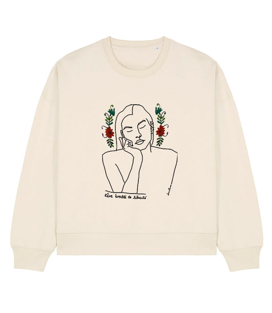 Mock-up d'un sweat en coton bio écru. Le vêtement présente un imprimé noir minimaliste d’un visage féminin aux yeux clos, accompagné de l’inscription « rêve éveillé de liberté »; ainsi qu'une broderie de fleurs. Modèle Thémis, conçu et imprimé à Lyon par la marque éthique Leonor Roversi.