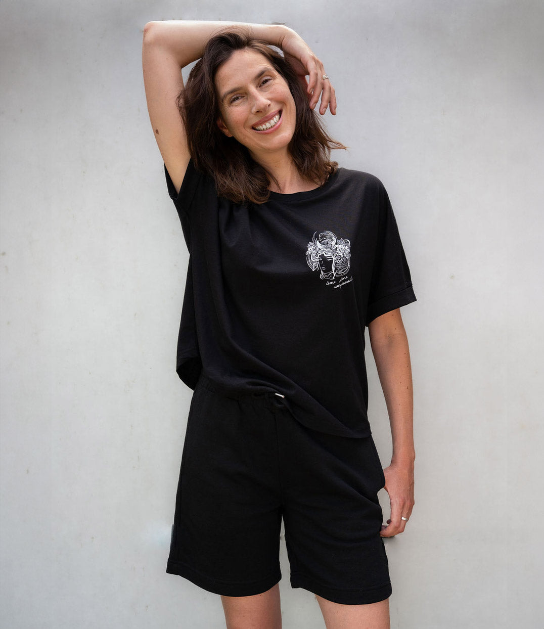 Femme souriante portant un ensemble décontracté avec un short noir en coton bio à taille élastique et lacets. Modèle Sekhmet, conçu et imprimé à Lyon par Leonor Roversi.