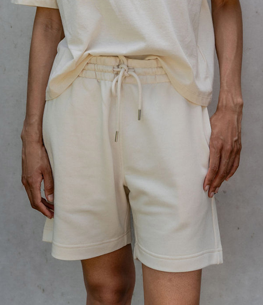 Femme portant un ensemble décontracté avec un short écru en coton bio à taille élastique et lacets. Modèle Sekhmet, conçu et imprimé à Lyon par la marque éthique Leonor Roversi.