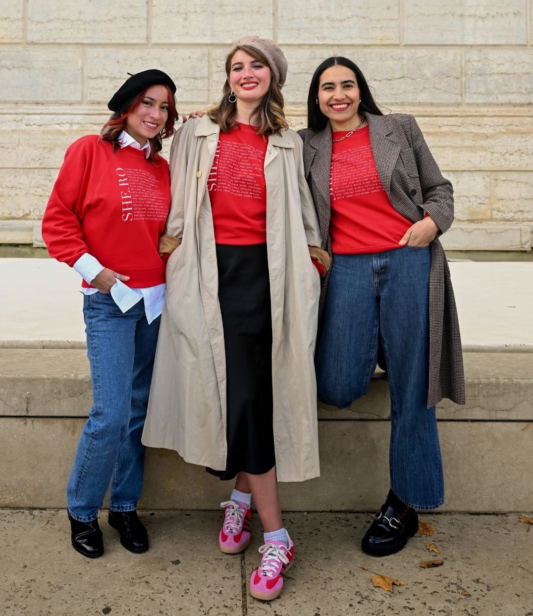 3 Femmes qui porte chacune un sweat Rouge shero de chez Leonor Roversi. SHE.RO comme HERO mais pour les femmes, héroïnes. Elles sont devant un mur en pierre et sont souriantes.