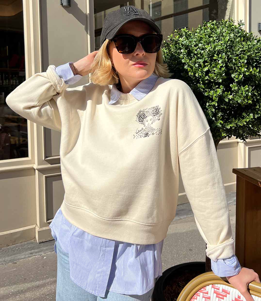 Femme portant un sweatshirt écru en coton biologique, imprimé noir d'une femme forte avec des fleurs dans les cheveux représentant la première reine nigériane accompagnée de l'inscription  "Valiente" sur le côté. Modèle Valiente conçu et imprimé à Lyon par la marque éthique Leonor Roversi.