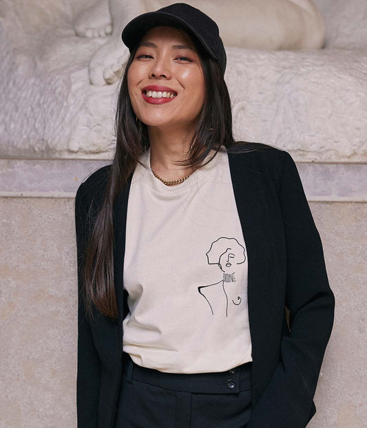 T-shirt écru pour femme en coton bio, porté face caméra, mettant en valeur le dessin noir d’une femme forte symbole de courage et de résilience. Sérigraphie éco-responsable réalisée à Lyon par la marque lyonnaise Leonor Roversi.