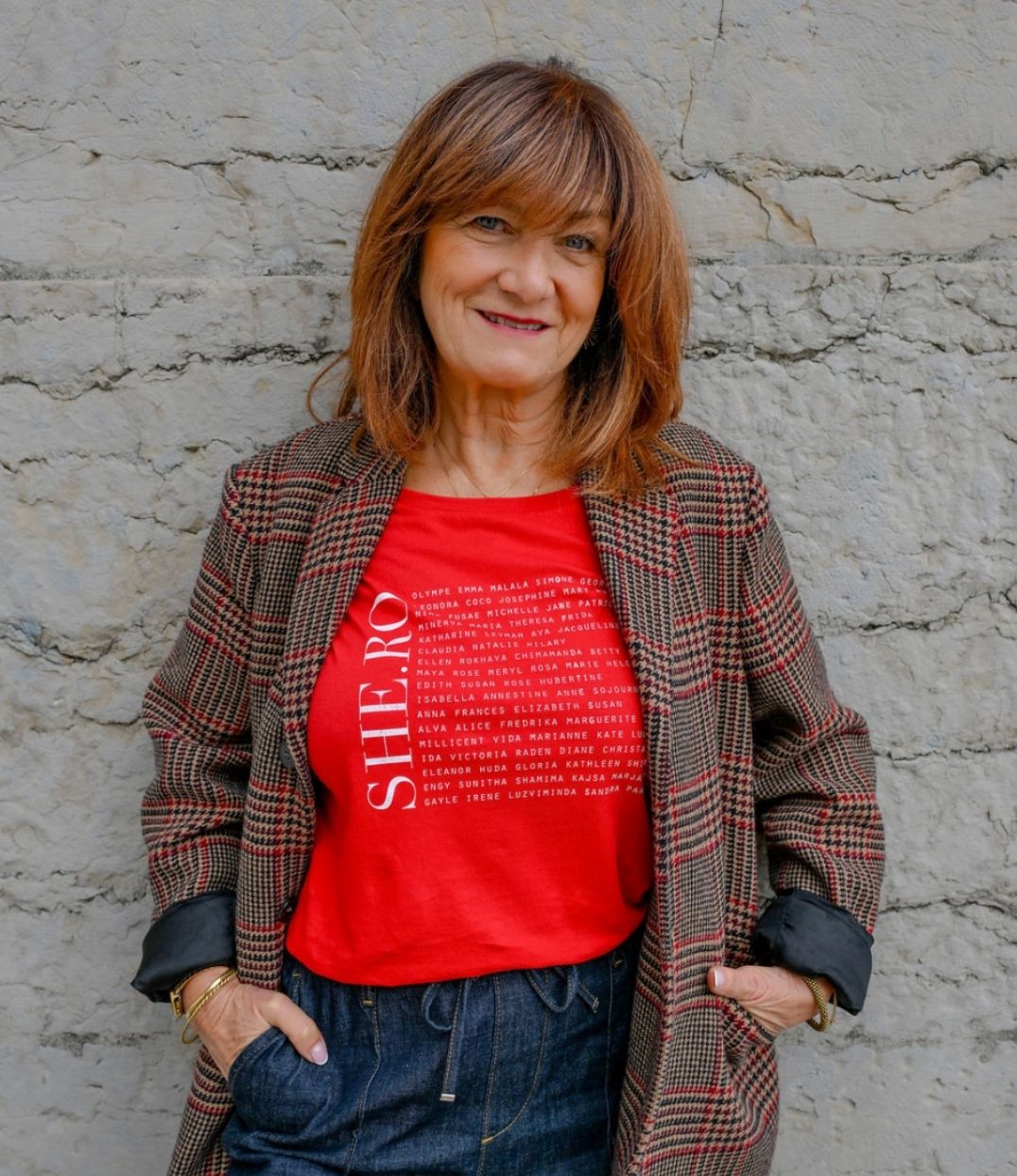 Femmes qui porte un t-shirt Rouge shero de chez Leonor Roversi. SHE.RO comme HERO mais pour les femmes, héroïnes. Elle est devant un mur en pierre.