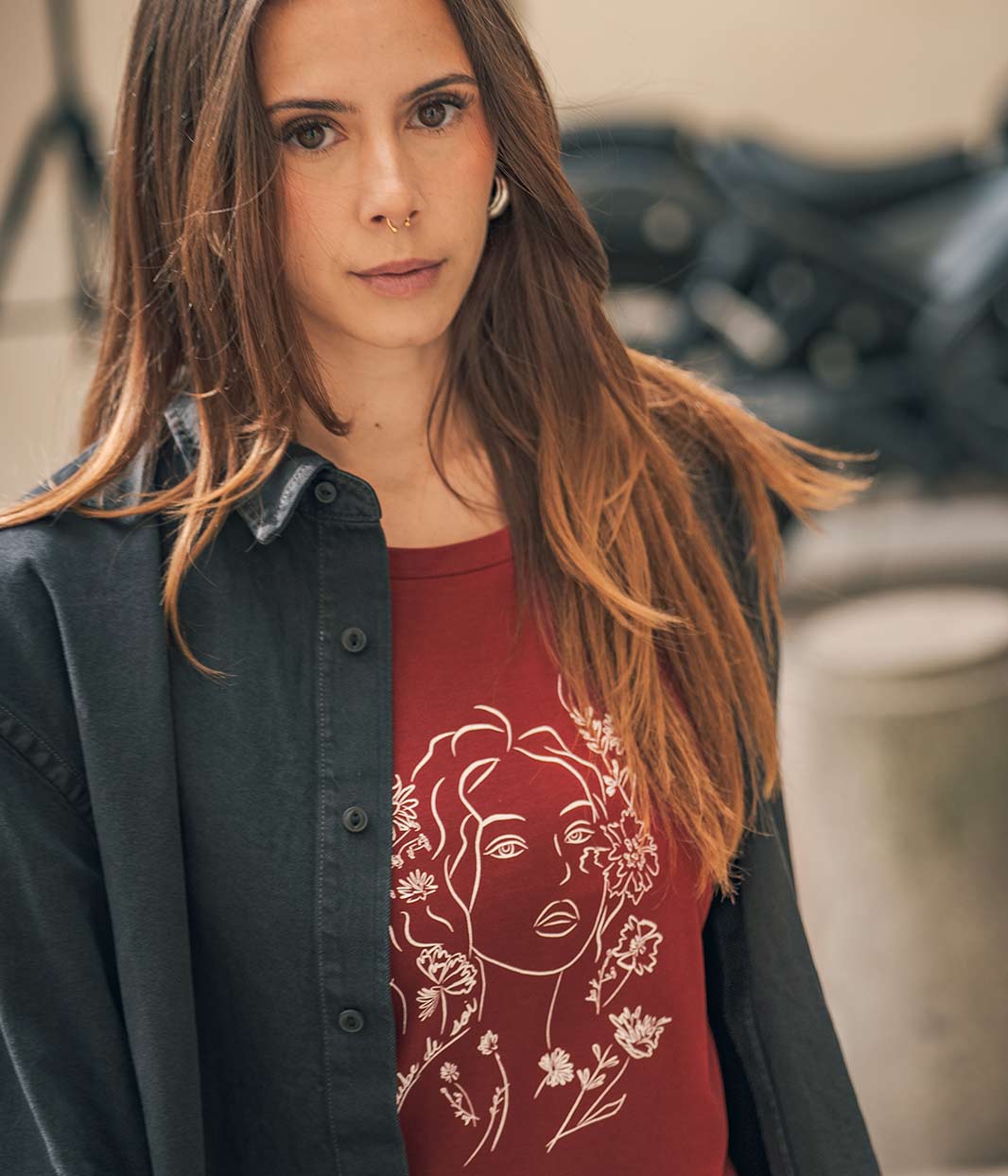 Mannequin femme regarde la caméra, elle porte une chemise noire en denim avec en dessous un t-shirt en coton bio, rouge, bordeaux avec un dessin dessus Leonor Roversi 