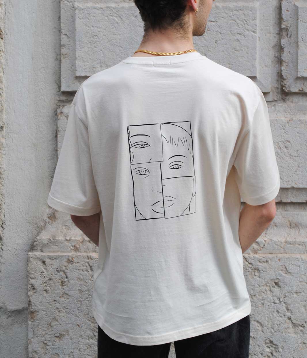 Personne photographiée de dos portant un t-shirt écru unisexe oversize en coton bio. Le vêtement présente un imprimé blanc au dos, représentant un visage fragmenté en lignes minimalistes, symbole de l’imperfection et de la pluralité des identités. Sérigraphie artisanale et éthique réalisée à Lyon par la marque lyonnaise Leonor Roversi, dans l’esprit de la philosophie japonaise Wabi Sabi.