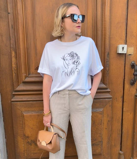 Femme portant un t-shirt en coton bio blanc, imprimé noir d’une femme inspirée de la peintre impressionniste Mary Cassatt représentant une femme au regard serein entourée de fleurs dans les cheveux accompagnée de l'inscription "Absolumente única". Modèle Unica, conçu et imprimé à Lyon par la marque éthique Leonor Roversi.