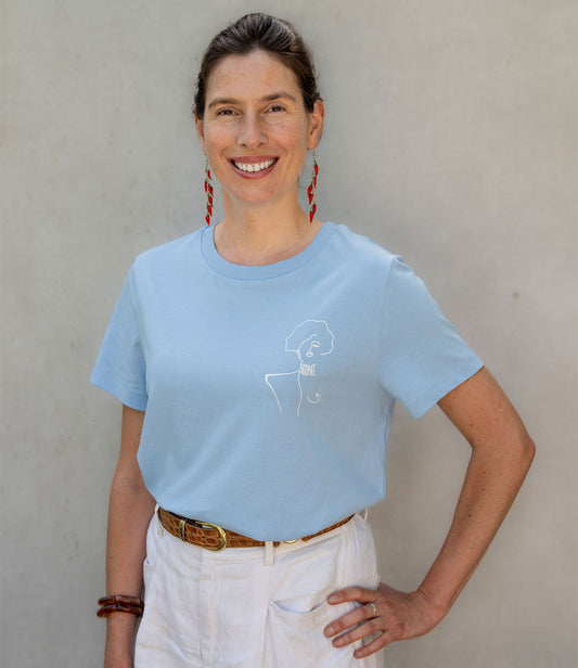 Femme souriante portant un t-shirt ample en coton bio bleu, imprimé blanc d'une femme forte avec l'inscription "battante". Modèle Klimt, conçu et imprimé à Lyon par la marque éthique Leonor Roversi.