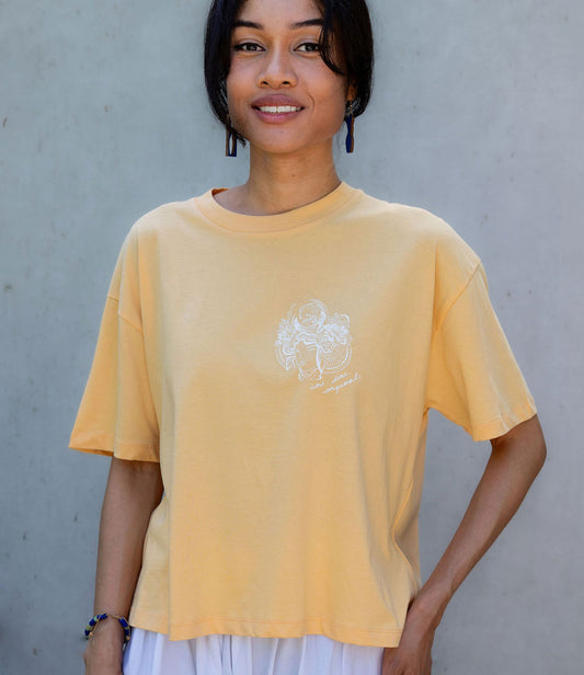 Femme souriante portant un t-shirt en coton bio melon, imprimé blanc représentant une femme samouraï avec l'inscription "âme d'une conquérante". Modèle Gozen, conçu et imprimé à Lyon par la marque éco-responsable Leonor Roversi