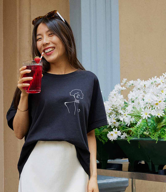 Femme souriante portant un t-shirt ample en coton bio noir, imprimé blanc d'une femme forte avec l'inscription "battante". Modèle Klimt, conçu et imprimé à Lyon par la marque éthique Leonor Roversi.