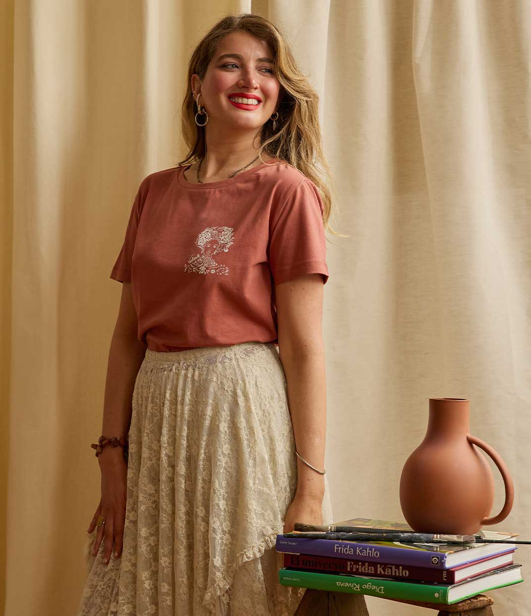 Une femme portant un t-shirt terracotta Valiente en coton biologique de Leonor Roversi, marque de mode responsable et artistique à Lyon, avec une illustration sérigraphiée rendant hommage à Amina de Zaria, symbole de courage et d’empowerment féminin.
