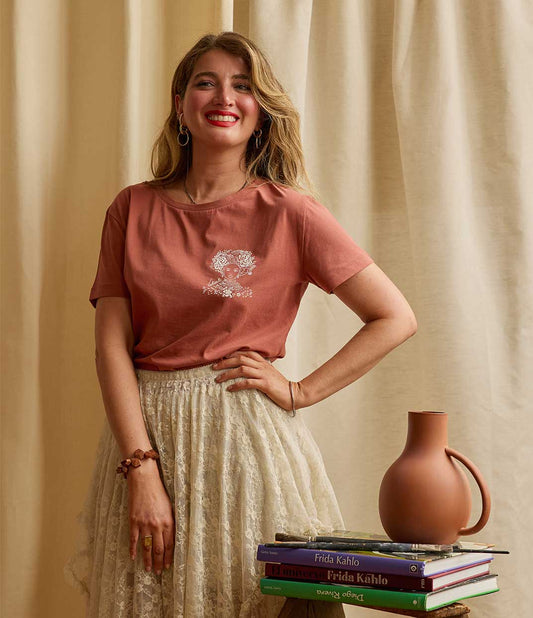 Une femme portant un t-shirt terracotta Valiente en coton biologique de Leonor Roversi, marque de mode éthique et féminine basée à Lyon, avec une illustration en sérigraphie artisanale rendant hommage à Amina de Zaria, figure de courage et de leadership féminin.