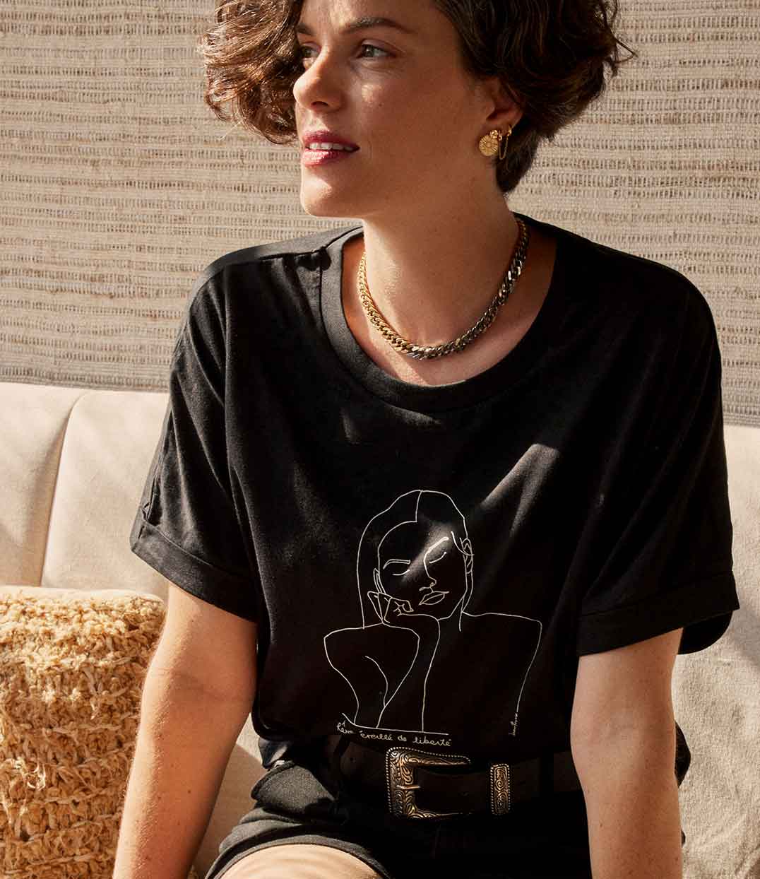 T-shirt noir minimaliste en coton bio certifié pour femme, avec un dessin épuré de Thémis, la déesse de la justice dans la mythologie grecque, centré sur la poitrine. Idéal pour un look élégant et symbolique.