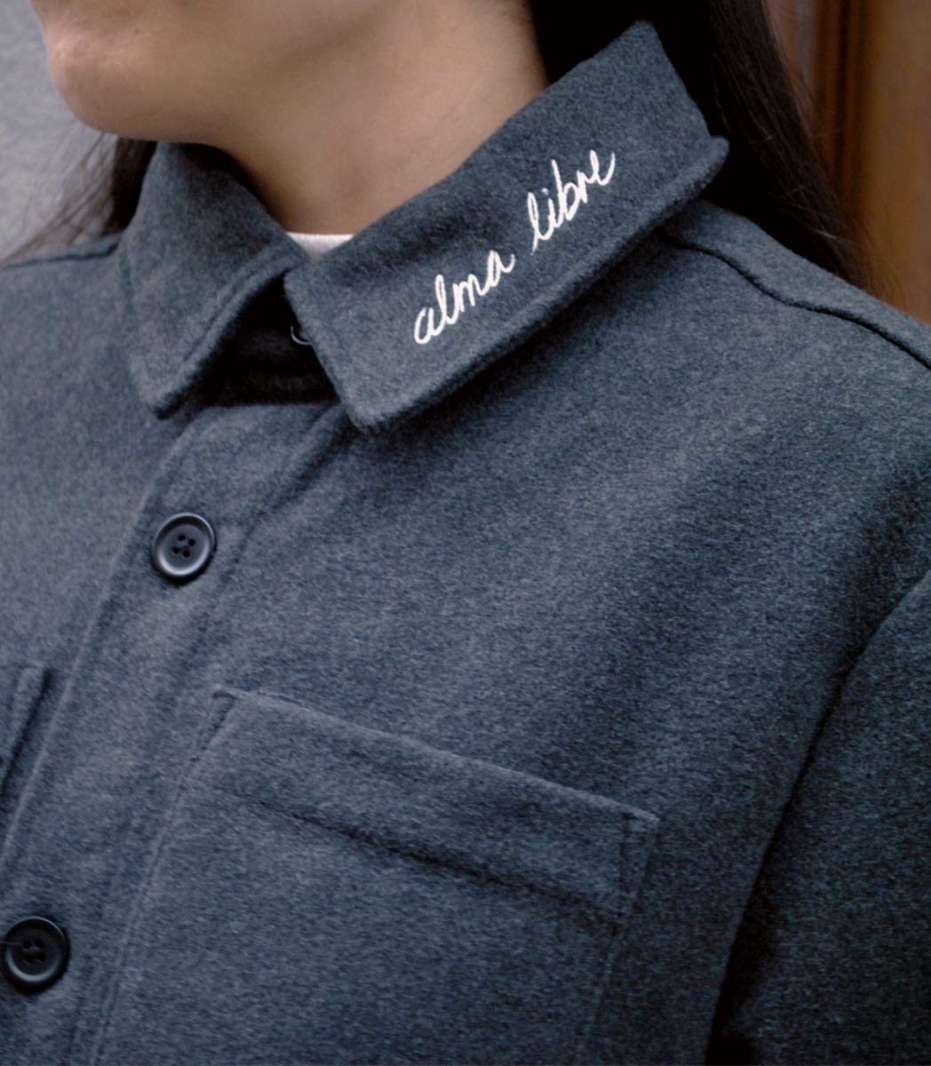 Veste ALMA LIBRE Leonor Roverssi en polyester recyclé certifié GOTS et FairWear, coupe droite gris foncé, portée par une femme confiante. Vêtement éthique brodé à Lyon, inspiré de la liberté intérieure et de la résilience féminine.