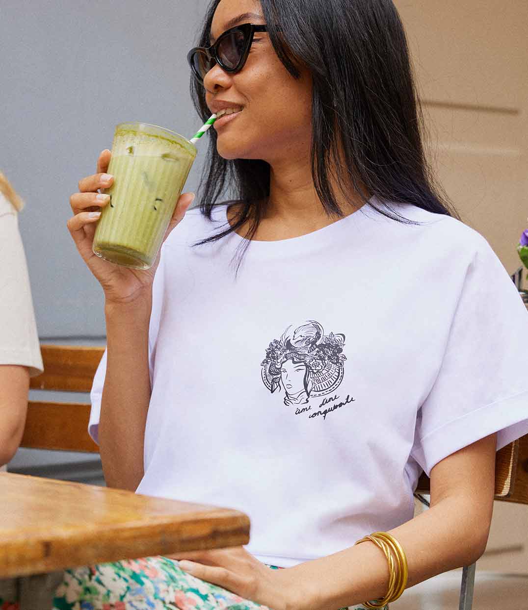 Gros plan sur un t-shirt pour femme en coton bio blanc. Il présente un imprimé noir représentant une figure de samouraï couronnée de fleurs, accompagné de l’inscription « âme d’une conquérante ». Modèle Gozen, conçu et imprimé à Lyon par la marque éthique Leonor Roversi.