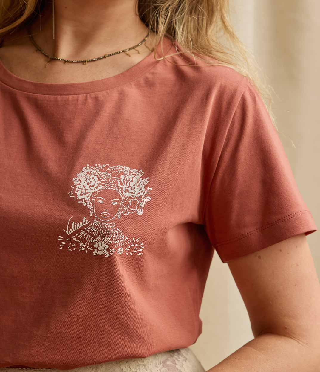 Gros plan sur une femme portant un t-shirt terracotta Valiente de Leonor Roversi en coton biologique, création de mode durable et féminine, sérigraphiée artisanalement à Lyon, mettant à l’honneur la reine Amina de Zaria, symbole de courage, de diversité et d’empowerment.