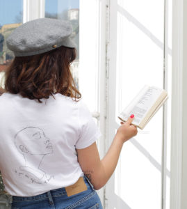 femme de dos qui lit un livre, elle porte un tshirt blanc en coton bio de la marque leonor roversi
