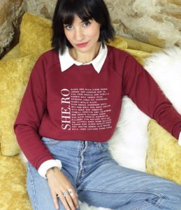 femme assise sur camapé portant un sweatshirt bordeaux avec ecritures feministe leonor roversi