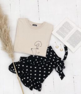 t-shirt aplat klimt beige en coton bio accompagné d'un livre d'une fleur séché et de boucle d'oreille et d'une jupe