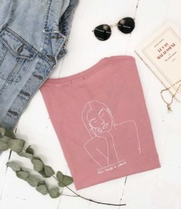 photo du t-shirt themis rose de la marque leonor roversi accompagné d'une veste en jean de lunettes de soleil d'un livre et d'une chaine